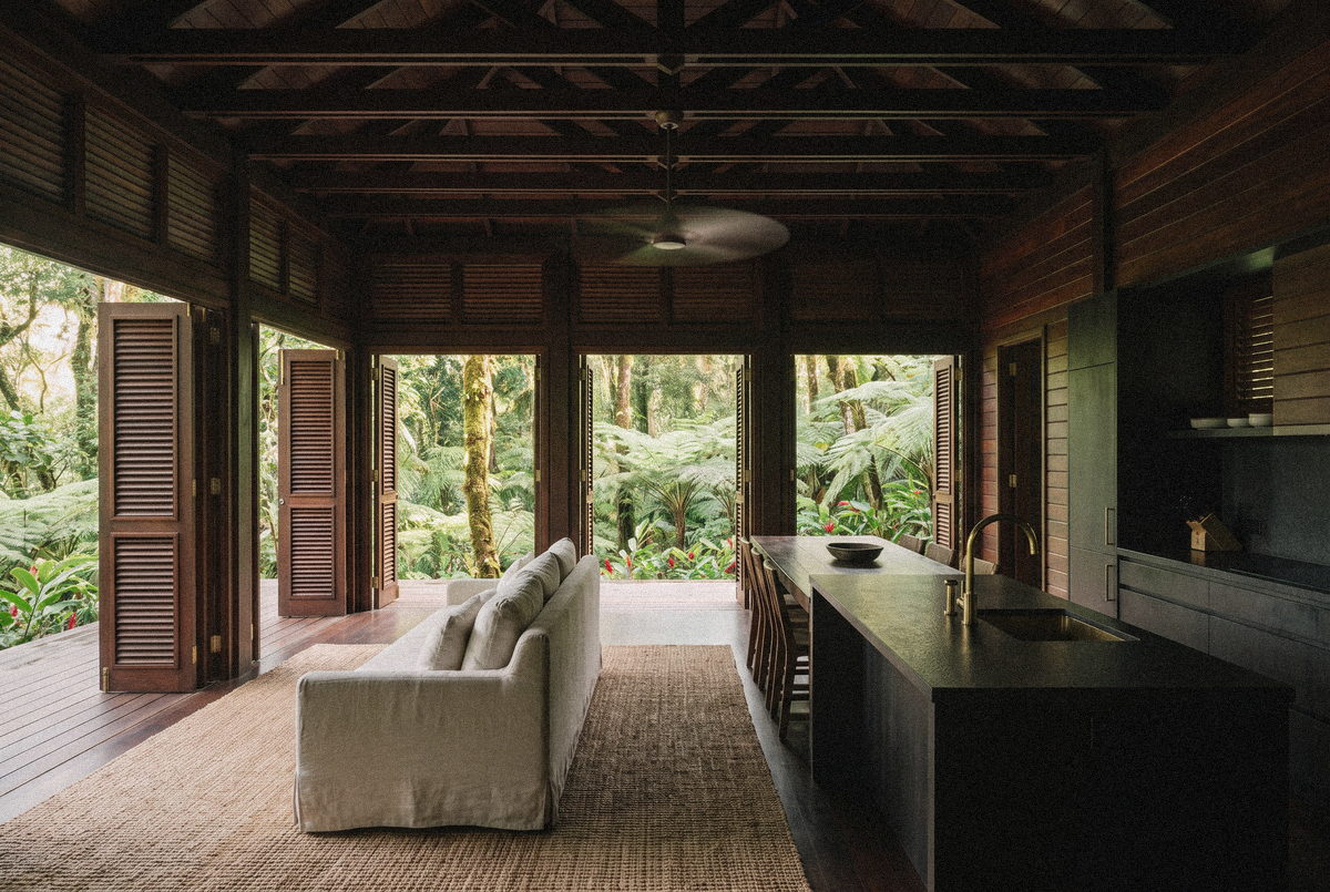 Séjour et cuisine ouverts de la Villa Rivière, bois sombre et lin, face à la terrasse.